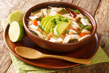 Homemade Caldo tlalpeno is a Mexican chicken soup topped with avocado and cheese close-up in a bowl on the table. horizontal