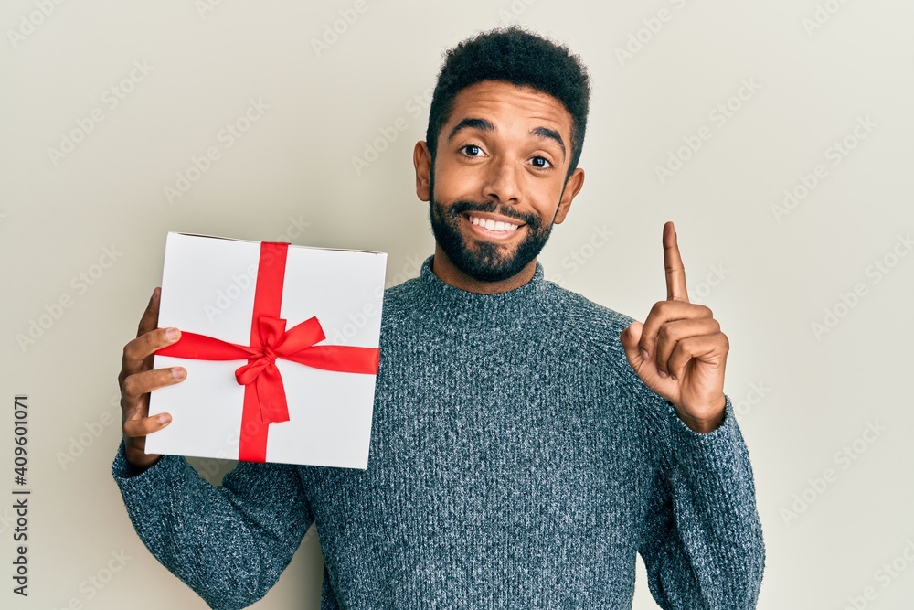 Sticker Handsome hispanic man with beard holding gift smiling with an idea or question pointing finger with happy face, number one