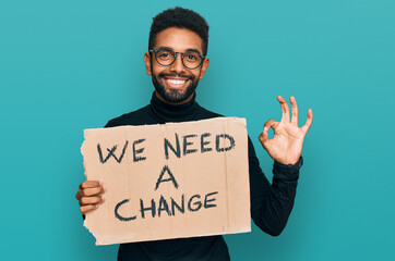 Young african american man holding we need a change banner doing ok sign with fingers, smiling friendly gesturing excellent symbol