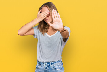 Beautiful young blonde woman wearing casual clothes and glasses covering eyes with hands and doing stop gesture with sad and fear expression. embarrassed and negative concept.