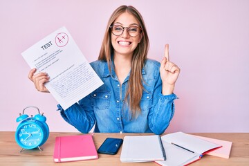 Young blonde girl showing passed exam sitting on the table smiling with an idea or question...