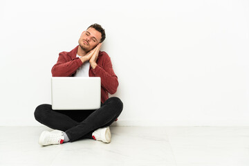 Young handsome caucasian man sit-in on the floor with laptop making sleep gesture in dorable expression