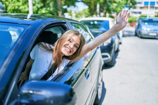 Young beautiful blonde woman smiling happy sitting at the car with hand out and cheerful expression
