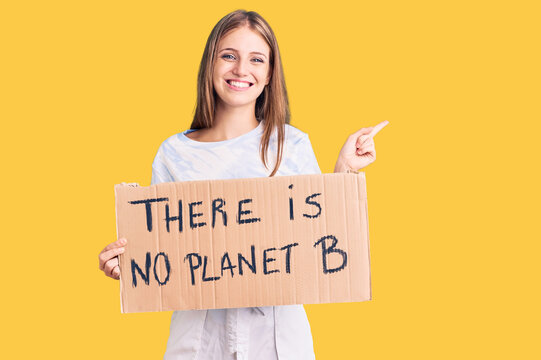 Young beautiful blonde woman holding there is no planet b banner smiling happy pointing with hand and finger to the side