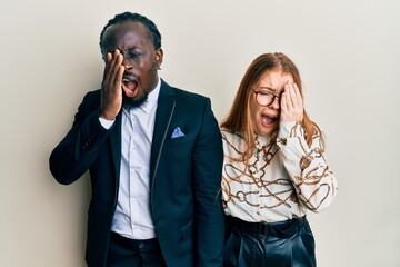Young interracial couple wearing business and elegant clothes yawning tired covering half face, eye and mouth with hand. face hurts in pain.