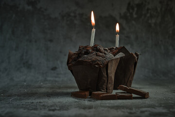 chocolate muffins on a dark background with a lit candle