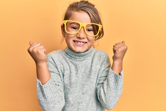 Little beautiful girl wearing casual clothes and yellow glasses screaming proud, celebrating victory and success very excited with raised arm