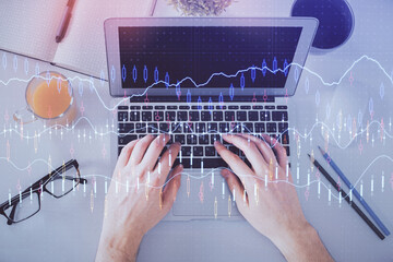 Double exposure of man's hands typing over laptop keyboard and forex chart hologram drawing. Top view. Financial markets concept.