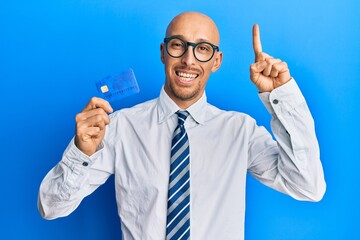 Bald man with beard holding credit card smiling with an idea or question pointing finger with happy...