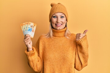 Middle age caucasian woman holding swiss franc banknotes smiling happy and positive, thumb up doing excellent and approval sign