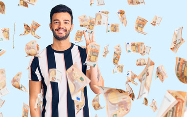 Young handsome hispanic man wearing striped tshirt showing and pointing up with fingers number three while smiling confident and happy.