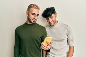 Homosexual gay couple standing together using smartphone looking positive and happy standing and smiling with a confident smile showing teeth