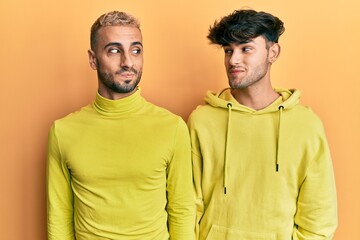 Obraz premium Homosexual gay couple standing together wearing yellow clothes smiling looking to the side and staring away thinking.