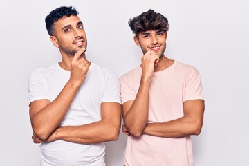 Young gay couple wearing casual clothes looking confident at the camera with smile with crossed arms and hand raised on chin. thinking positive.