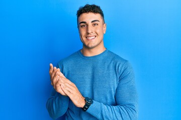 Hispanic young man wearing casual winter sweater clapping and applauding happy and joyful, smiling proud hands together