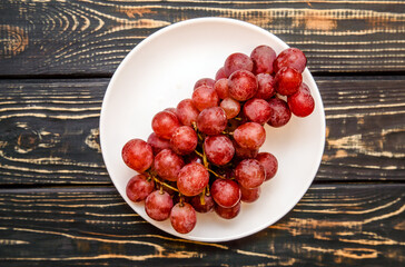 Branch of red grapes lies on a brown wooden background
