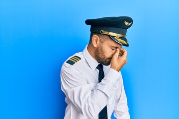 Handsome man with beard wearing airplane pilot uniform tired rubbing nose and eyes feeling fatigue...