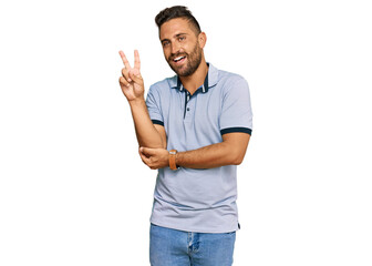 Handsome man with beard wearing casual clothes smiling with happy face winking at the camera doing victory sign with fingers. number two.