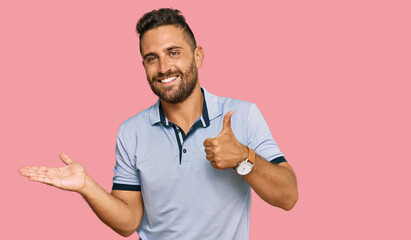 Handsome man with beard wearing casual clothes showing palm hand and doing ok gesture with thumbs up, smiling happy and cheerful