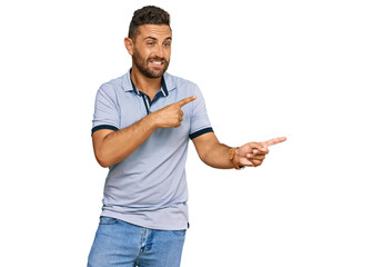 Handsome man with beard wearing casual clothes pointing aside worried and nervous with both hands,...