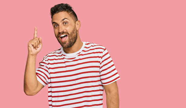 Handsome man with beard wearing striped tshirt pointing finger up with successful idea. exited and happy. number one.