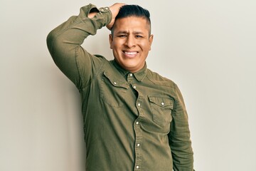 Young latin man wearing casual clothes smiling confident touching hair with hand up gesture, posing attractive and fashionable