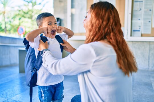 Adorable latin student boy and mom at school. Mother preparing kid putting up backpack.