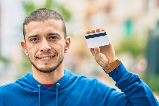 Young hispanic man smiling happy holding credit card at the city