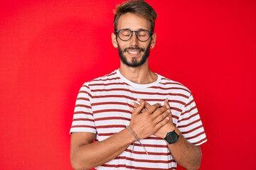Handsome caucasian man with beard wearing casual clothes and glasses smiling with hands on chest with closed eyes and grateful gesture on face. health concept.