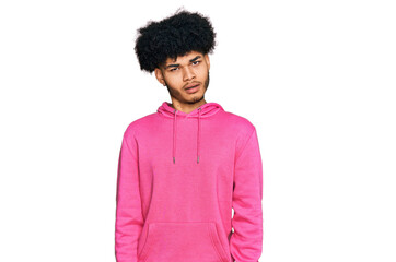 Young african american man with afro hair wearing casual pink sweatshirt in shock face, looking...