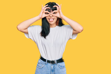 Young hispanic girl wearing casual clothes doing ok gesture like binoculars sticking tongue out, eyes looking through fingers. crazy expression.