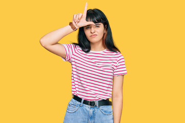 Young hispanic girl wearing casual clothes making fun of people with fingers on forehead doing...