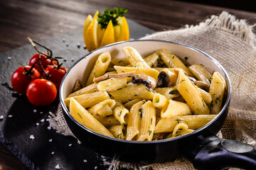 Penne with roast chicken meat, cream sauce, parmesan cheese and vegetables served on wooden table in pan
