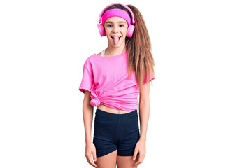 Obraz na płótnie Canvas Cute hispanic child girl wearing gym clothes and using headphones sticking tongue out happy with funny expression. emotion concept.