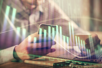 Double exposure of man's hands holding and using a phone and financial graph drawing. Analysis concept.