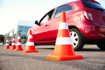 Traffic cones near red car outdoors. Driving school exam