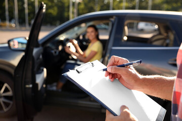 Instructor with clipboard near car outdoors, closeup. Driving school exam