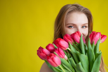Fototapeta premium Woman with a bouquet of red tulips on a yellow background. Happy girl in a black dress holds an armful of flowers . Gift for Valentine's Day. The most romantic day of the year.