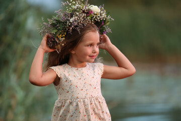 Cute little girl wearing wreath made of beautiful flowers outdoors