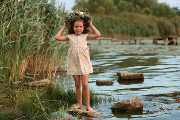 Cute little girl wearing wreath made of beautiful flowers near river