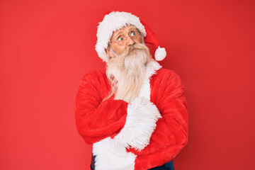 Old senior man with grey hair and long beard wearing traditional santa claus costume smiling looking to the side and staring away thinking.
