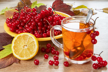 Tea with viburnum berries and lemon, viburnum berries in a bowl, on a wooden table. Still life with red viburnum.