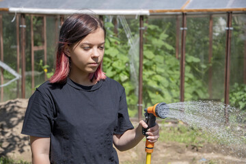 Portrait of a 17-year-old teenage girl watering a vegetable garden with water from a watering hose. Concept: caring for the crop.