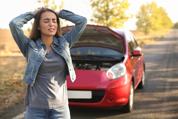Stressed young woman near broken car outdoors