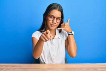 Beautiful hispanic woman wearing casual clothes sitting on the table smiling doing talking on the...