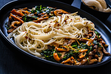 Asian food - fried soy sauce oyster mushrooms with noodles on black stone
