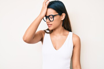 Young beautiful latin girl wearing casual clothes and glasses surprised with hand on head for mistake, remember error. forgot, bad memory concept.