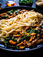 Asian food - fried soy sauce oyster mushrooms with noodles on black stone
