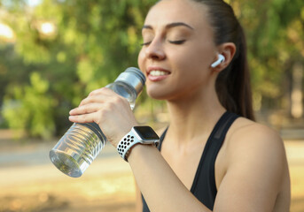 Woman with modern smart watch drinking water outdoors