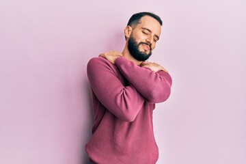 Young man with beard wearing casual winter sweater hugging oneself happy and positive, smiling confident. self love and self care